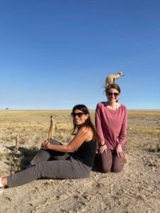Two women with Meerkats sitting on them in South Africa.