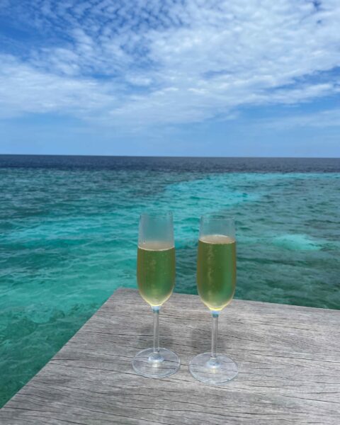 Two champagne glasses on a table by the water at Patina Maldives Resort.