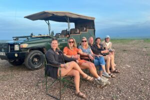 A group on safari sitting near a jeep.
