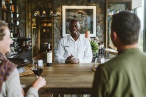 Person smiling in front of two other people drinking wine