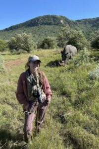 Woman smiling with a rhino in the distant background.