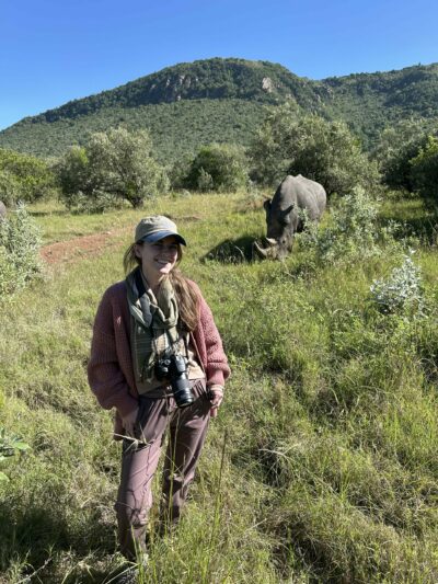 Woman smiling with a rhino in the distant background.