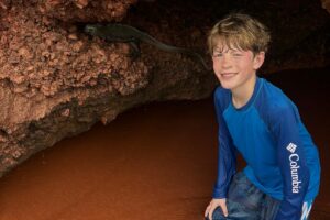 A boy kneeling by a Galapagos Marine Iguana.