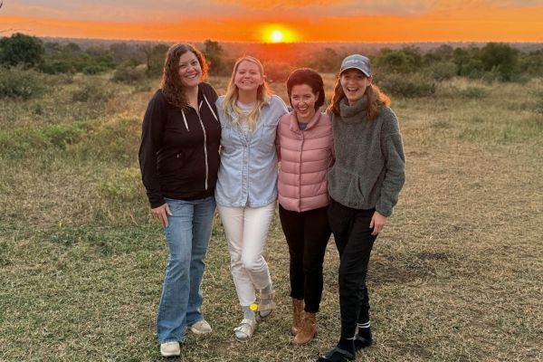 Four women smiling in front of a sunset in Africa.