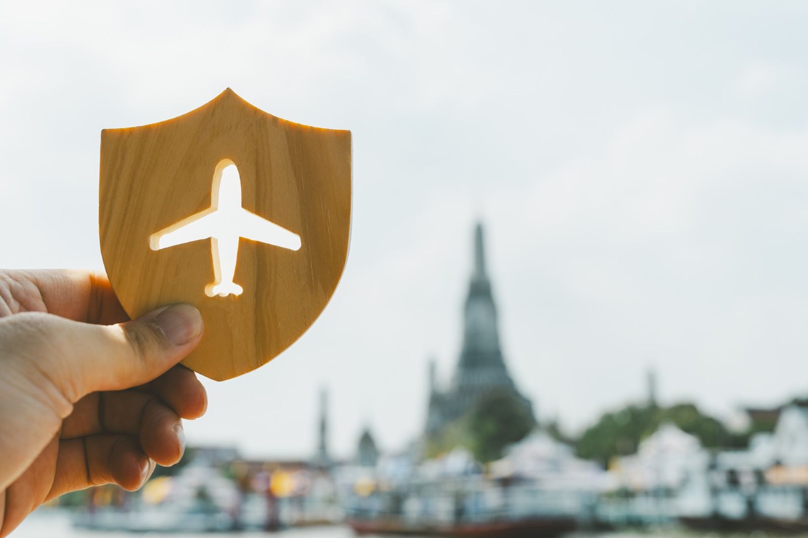 Person holding up travel insurance icon in front of city.