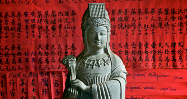 A statue of the Goddess of Mercy, Thien Hau, in front of a wall of chinese characters on vibrant red paper at Phuc Kien pagoda in Hoi An.