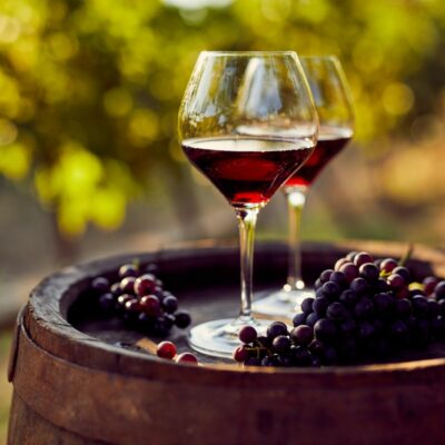 Two glasses of red wine and grapes sitting on top of a wine barrel.